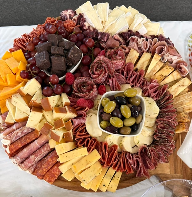 Round charcuterie board with cheeses, fruit, meats, and olives