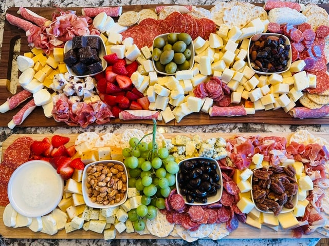 Two generously arranged charcuterie boards with cheeses, meats, fruit, and crackers